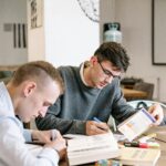 Zwei Männer lernen gemeinsam an einem Tisch mit Büchern und Notizen für den ITIL-Version-5-Übergang