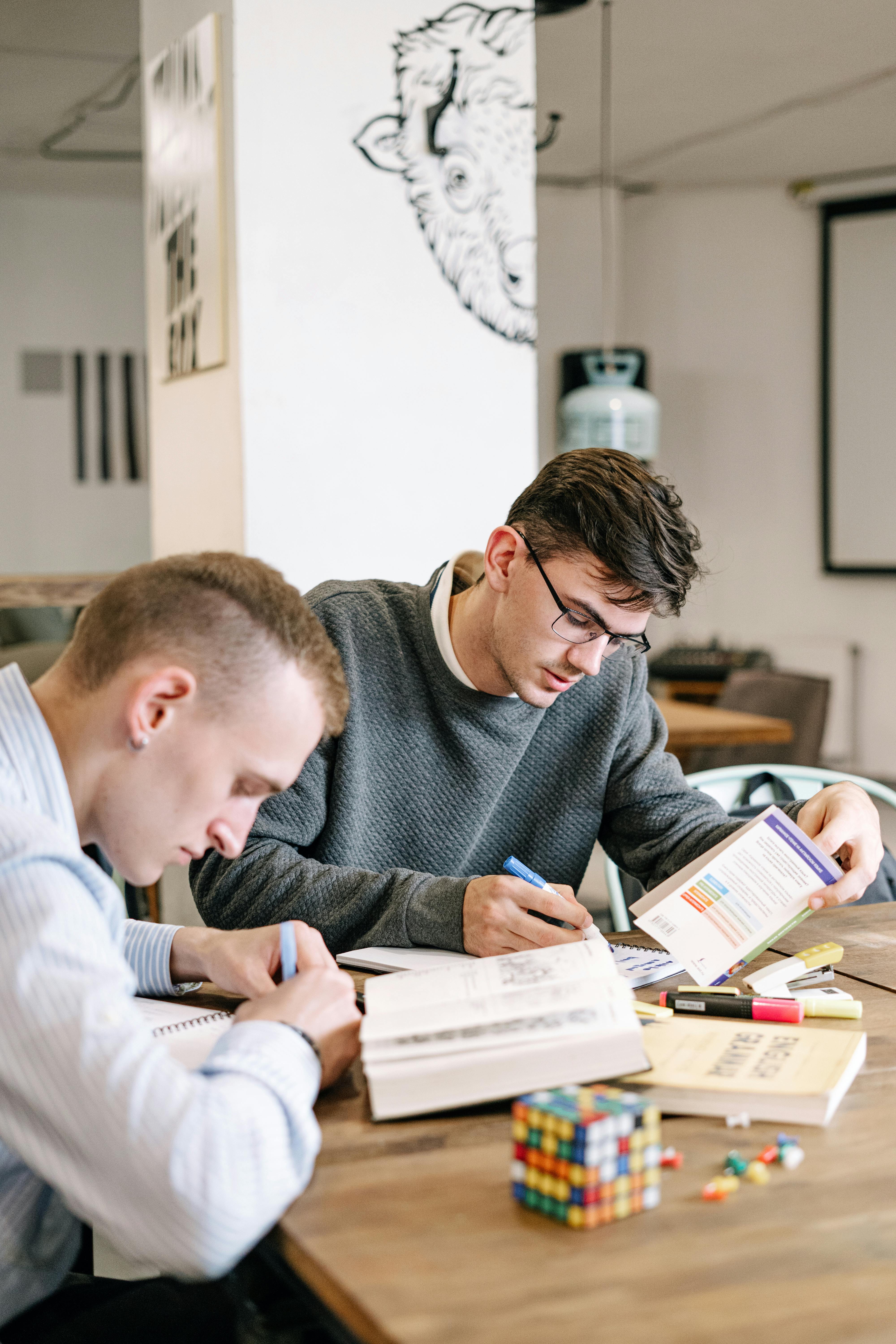 Zwei Männer lernen gemeinsam an einem Tisch mit Büchern und Notizen für den ITIL-Version-5-Übergang