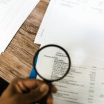 A person using a magnifying glass on a document for audit and service evidence review