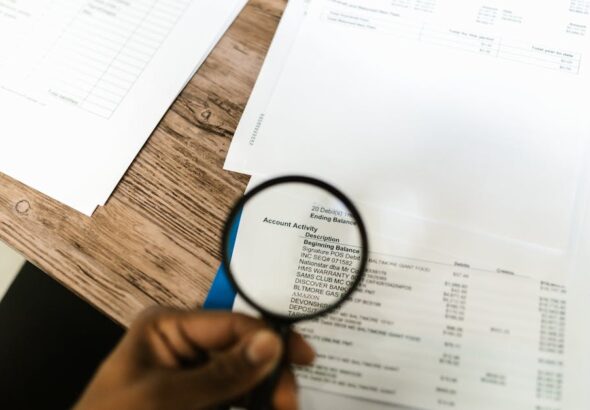 A person using a magnifying glass on a document for audit and service evidence review