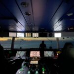 Eine Person auf einer Schiffsbrücke überwacht Instrumente als Symbol für gesteuerte Rollouts, Beobachtung und Feature-Flag-Entscheidungen im DevOps-Betrieb