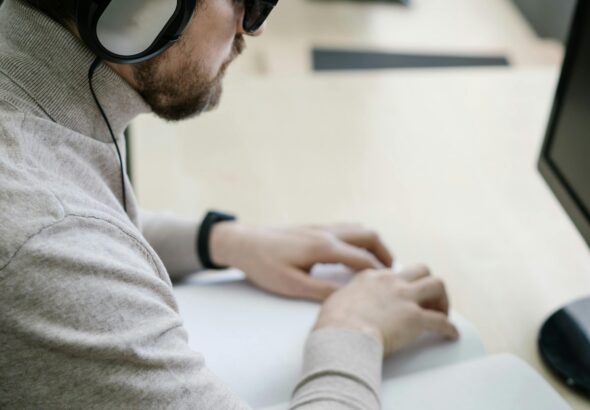 Blinder Mann mit Braille-Unterlagen und Computer im Büro als Symbol für barrierefreie digitale Serviceportale